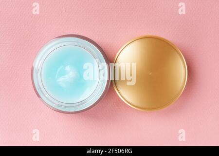 Feuchtigkeitsspendendes Gesichtsgel in einem offenen Glas und goldenem Deckel auf einem pastellrosa Hintergrund. Glasbehälter aus blau feuchtigkeitsspendenden Gesichtscreme. Schönheit, Hautpflege. Stockfoto