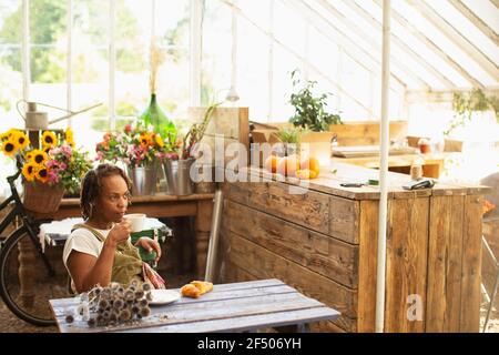 Weibliche Floristin, die Kaffeepause im Gewächshaus des Blumengeschäftes nimmt Stockfoto