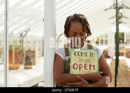 Portrait weibliche Gartencenter Besitzer mit offenem Schild im Gewächshaus Stockfoto