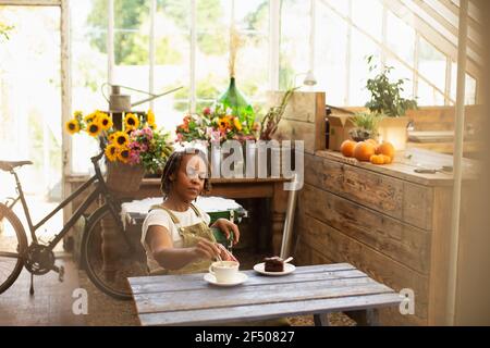 Weibliche Floristin genießen Kaffeepause am Tisch im Blumenladen Stockfoto
