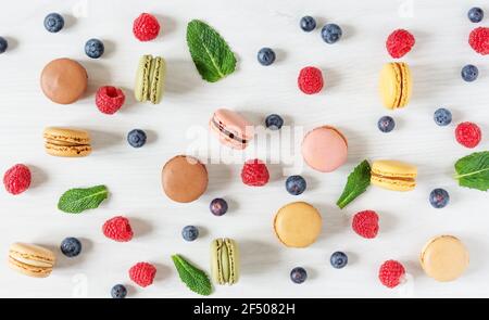 Hintergrund von bunten französischen Makronen und Beeren wie Himbeere und Heidelbeere und Minze Blätter Draufsicht. Französisch Meringue Cookie Makronen und Stockfoto