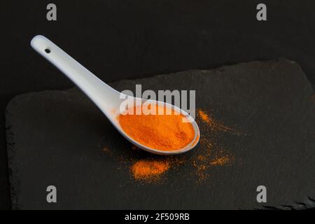 Ein Keramiklöffel mit Safran in Pulverform auf einem Schiefertisch Mit dunklem Hintergrund und Kopierbereich Stockfoto
