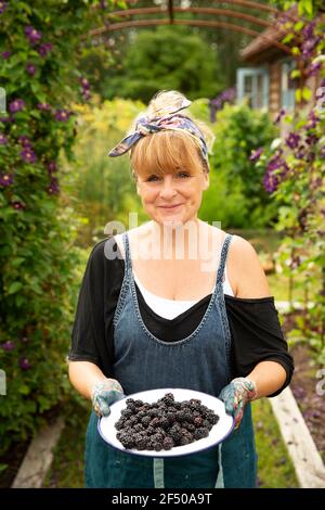 Portrait stolze Frau mit frisch geernteten Brombeeren im Garten Stockfoto