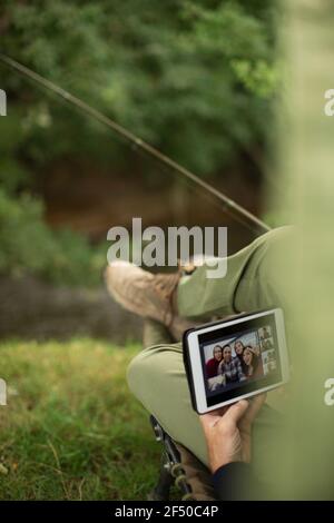 Mann Angeln und Video-Chat mit digitalen Tablet am Flussufer Stockfoto