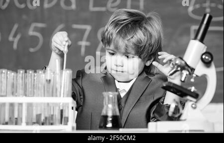 Kleiner Junge mit Mikroskop am Unterricht. Teströhrchen mit Flüssigkeit für die Forschung. Lernen für die Zukunft. Biologie Wissenschaft. Ergebnis. Medizinisches Konzept. Wenig Stockfoto