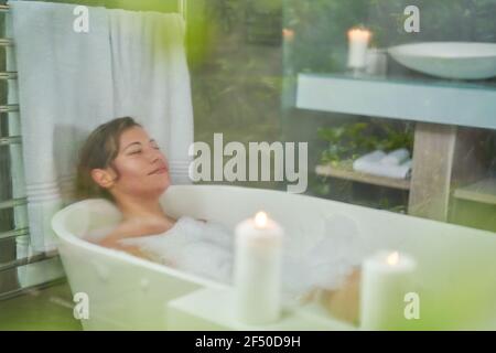 Heitere Frau genießen Schaumbad mit Kerzen im Luxus-Badezimmer Stockfoto