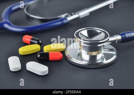 Stethoskop und verschiedene Tabletten, Tabletten und Kapseln auf einer schwarzen Oberfläche. Diagnose- und Behandlungskonzept. Stockfoto