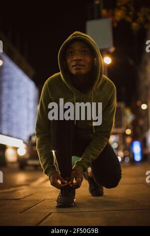 Junge Läuferin, die nachts auf dem städtischen Bürgersteig Schuhe schnürt Stockfoto