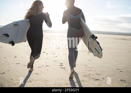 Unbeschwerte junge Surferinnen laufen am sonnigen Strand mit Surfbrettern Stockfoto