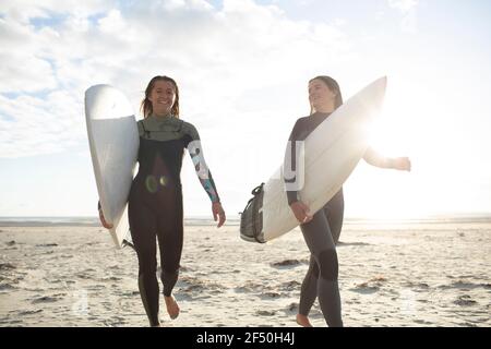 Fröhliche junge Surferinnen, die mit Surfbrettern am sonnigen Strand laufen Stockfoto