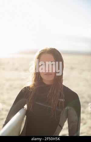 Portrait schöne junge Surferin mit nassem Haar auf sonnigen Strand Stockfoto
