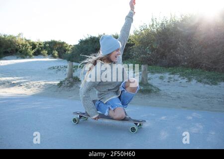 Sorglose junge Frau Skateboarding auf Strandweg Stockfoto