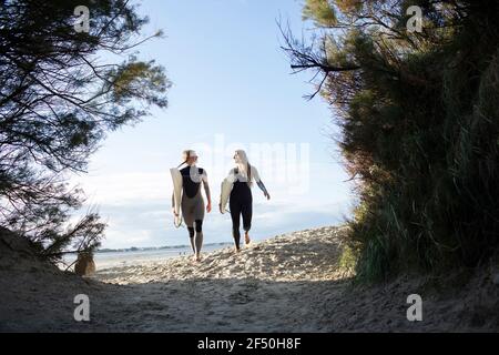 Junge Surferinnen wandern mit Surfbrettern auf sonnigem Strandweg Stockfoto