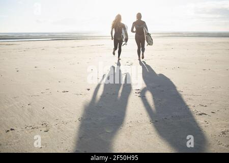Surferinnen laufen mit Surfbrettern am sonnigen idyllischen Strand Stockfoto