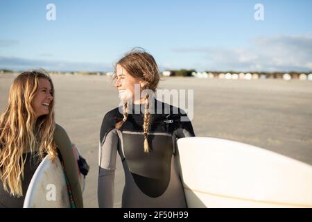 Glückliche junge Surferinnen, die Surfbretter am sonnigen Strand tragen Stockfoto