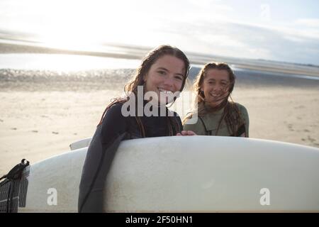 Portrait glückliche junge Surferinnen mit Surfbrett am sonnigen Strand Stockfoto