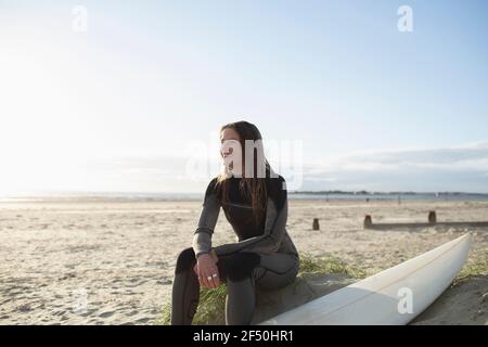 Glückliche junge Surferin, die mit Surfbrett am sonnigen Strand ruht Stockfoto