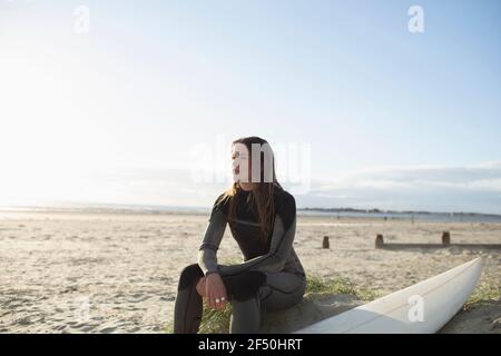 Ruhige schöne junge Surferin, die sich am sonnigen Sommerstrand ausruhen kann Stockfoto