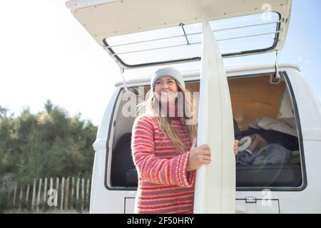 Glückliche junge Surferin mit Surfbrett auf der Rückseite des Camper Van Stockfoto