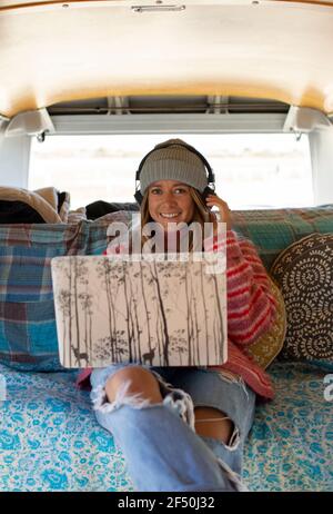 Portrait glückliche junge Frau mit Kopfhörer und Laptop im Wohnmobil Van Stockfoto