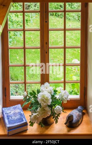 Stapel von Büchern, weißen Blumen und hölzernen Entenköcheln auf Glasfenstern unter der Treppe in einem alten, ca. 1735 kanadischen Haus Stockfoto