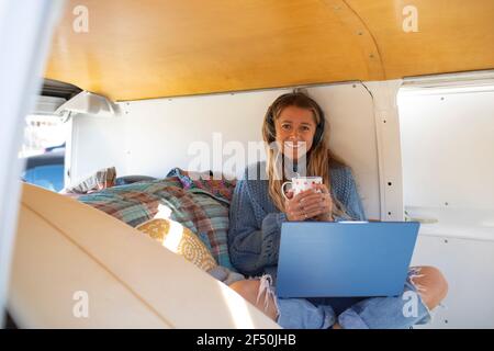 Portrait glückliche junge Frau mit Laptop Tee trinken in van Stockfoto