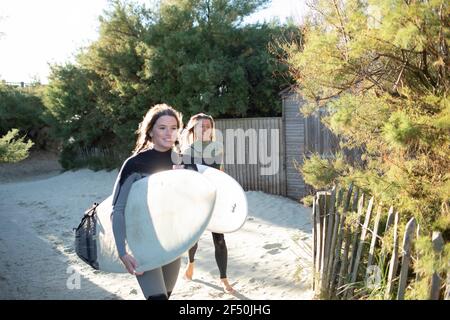 Junge Surferinnen mit Surfbrettern auf sonnigem Strandweg Stockfoto