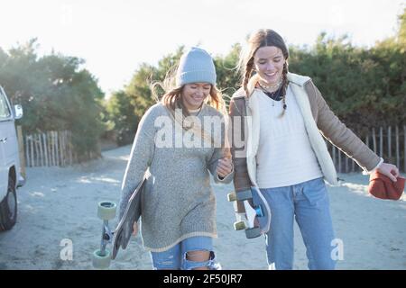 Glückliche junge Frauen Freunde mit Skateboards auf sonnigen Strandweg Stockfoto