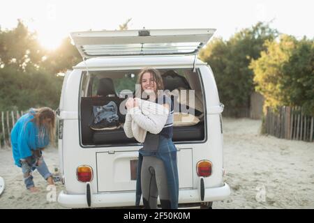 Portrait junge weibliche Surfer setzen auf Pullover bei sonnigen Camper Van Stockfoto