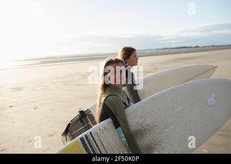 Portrait glückliche junge Surferinnen mit Surfbrettern am sonnigen Strand Stockfoto