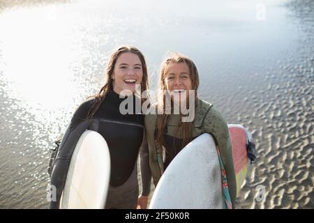 Portrait glückliche junge Surferinnen mit Surfbrettern am nassen Strand Stockfoto
