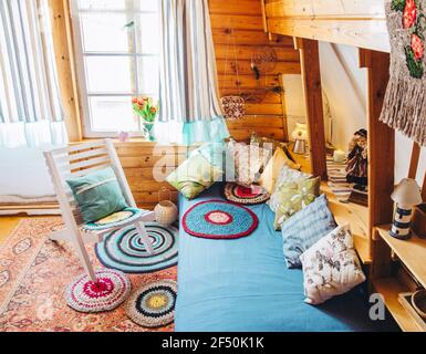 Maximalismus/maximalistisches Home-Konzept. Ferienhaus Hütte Schlafzimmer mit natürlichen Holzbrettwänden und Decke und viele verschiedene Farbdetails. Stockfoto