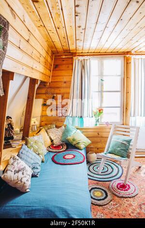 Maximalismus/maximalistisches Home-Konzept. Ferienhaus Hütte Schlafzimmer mit natürlichen Holzbrettwänden und Decke und viele verschiedene Farbdetails. Stockfoto