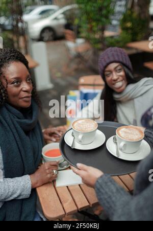 Kellnerin, die Mutter und Tochter Cappuccino serviert, im Straßencafé Stockfoto