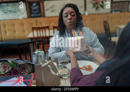 Mutter bläst Geburtstagskerze auf Kuchen im Restaurant mit Tochter Stockfoto