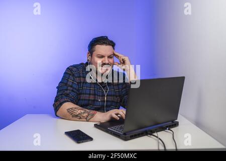 Junger tätowierter Mann, der an seinem Laptop arbeitet und lächelt Stockfoto