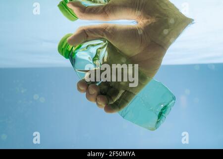 Beschnittene Ansicht der männlichen Hand mit Plastikflasche in Wasser, Ökologie Konzept Stockfoto