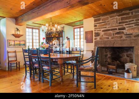 Esstisch aus Kiefernholz mit zwei Kapitänssesseln und sechs Stühlen mit hoher Rückenlehne, antikes Buffet aus Kiefernholz und Kamin aus Naturstein Stockfoto