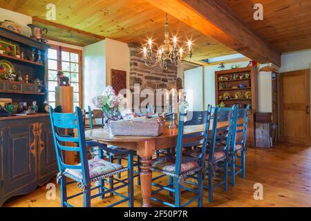 Esstisch aus Kiefernholz mit zwei Kapitänssesseln und sechs Stühlen mit hoher Rückenlehne, antikes Buffet aus Kiefernholz und Kamin aus Naturstein Stockfoto