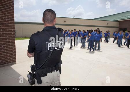 Pharr, TX USA 13. Mai 2010: High School Studenten im Pharr-San Juan-Alamo Schulbezirk mischen sich draußen, während sie auf ihre Schulbusse warten, beobachtet von einem lokalen Polizeibeamten, der der Sicherheitsabteilung der Schule im äußersten Süden von Texas zugewiesen wurde. Die Schüler müssen die blauen Uniformen während des Schultages tragen. ©Bob Daemmrich Stockfoto