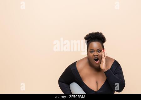 afroamerikanische plus size Frau in Sportbekleidung halten Fitness-Matte Und Geschrei isoliert auf beige Stockfoto