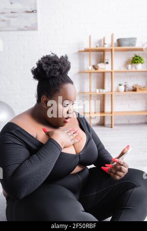 Schockiert afroamerikanischen plus size Frau in Sportkleidung Blick auf Smartphone Stockfoto