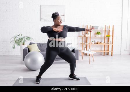 Volle Länge zufrieden african american plus size Frau in Sportbekleidung Training im Wohnzimmer Stockfoto