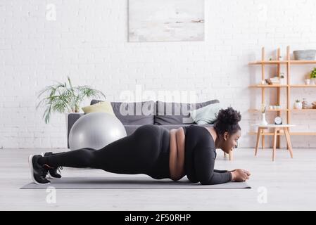 Seitenansicht der afroamerikanischen plus size Frau in Sportswear Dielenbrett im Wohnzimmer Stockfoto