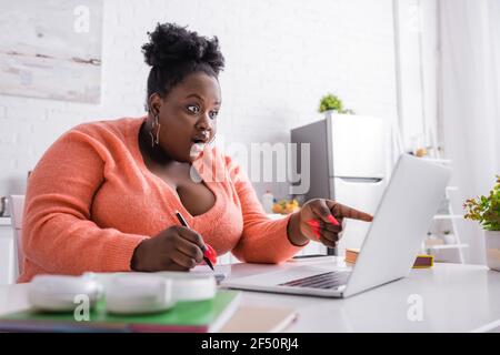 Schockiert afroamerikanischen plus size Freelancer zeigt mit dem Finger auf Notebook Stockfoto