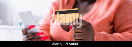 Teilansicht der afroamerikanischen plus size Frau mit Kreditkarte und Smartphone, Banner Stockfoto