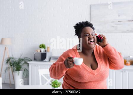 Happy african american plus size Frau im Gespräch auf Smartphone und Tasse Kaffee halten Stockfoto