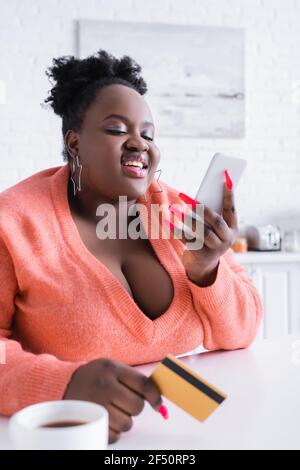 Lächelnd afroamerikanisch plus size Frau mit Kreditkarte und Smartphone Stockfoto