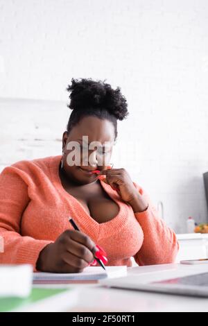 Nachdenkliche afrikanisch-amerikanische plus size Frau mit Schreiben im Notizbuch Stockfoto