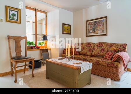 Rot, beige, grau kariertes Schlafsofa mit blumigen Sitz- und Rückenlehnen-Kissen, Holzcouchtisch und Hochlehnenstuhl mit genietetem schwarzem Ledersitz Stockfoto